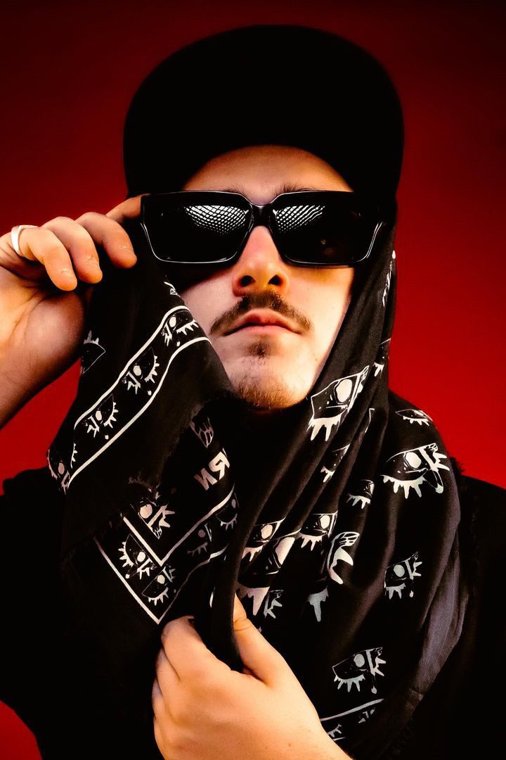 ALVA DJ adjusting his sunglasses, wearing a black paisley bandana over a cap
