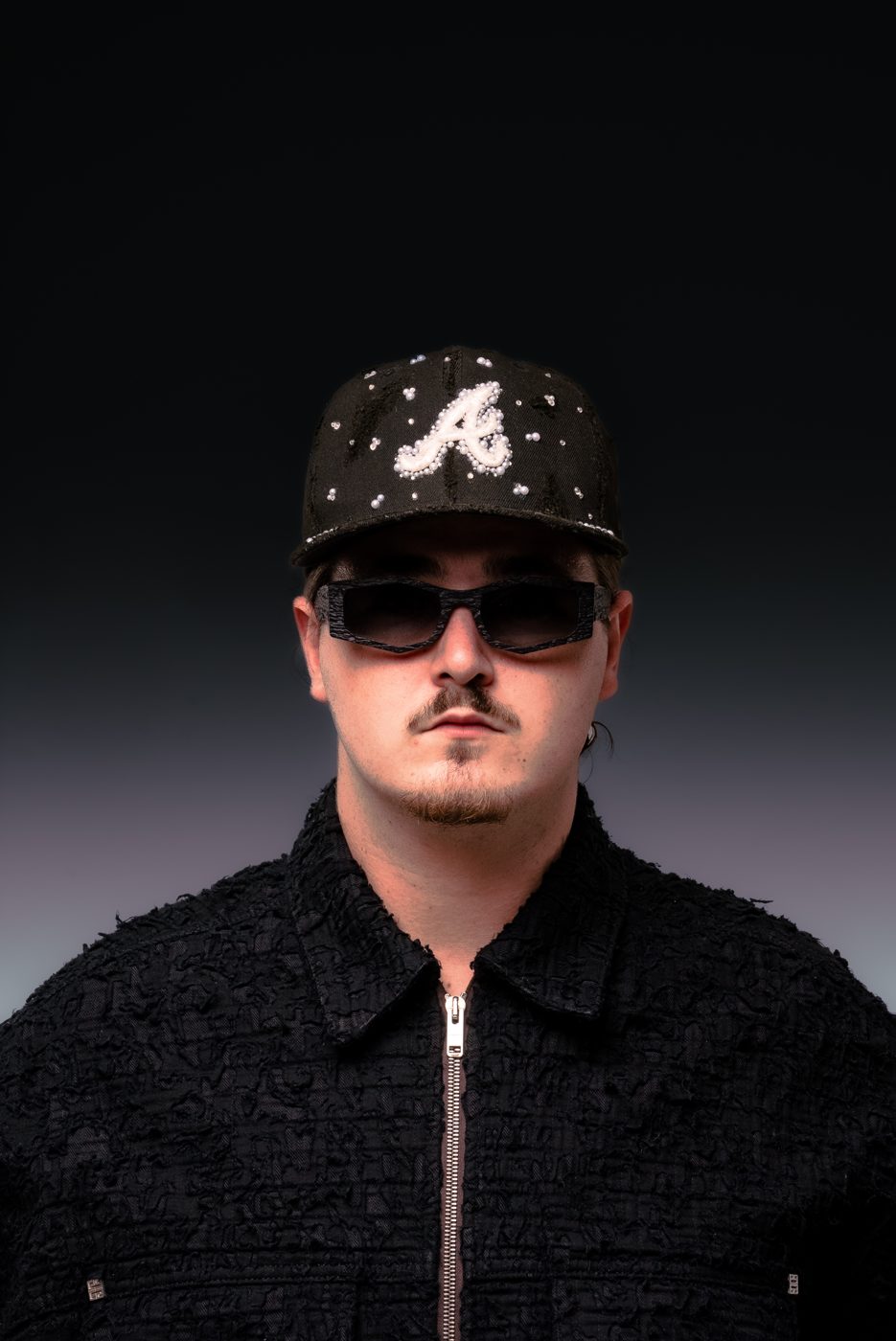 ALVA DJ in a studded cap and sunglasses, facing the camera